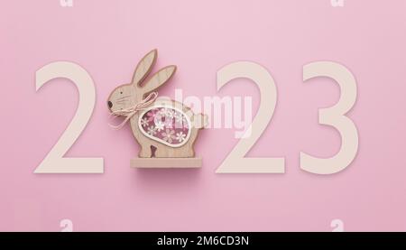 In celebration of Easter or the Chinese New Year 2023, the year of the Rabbit. A wooden rabbit on a pink background displaying the number 2023. Stock Photo