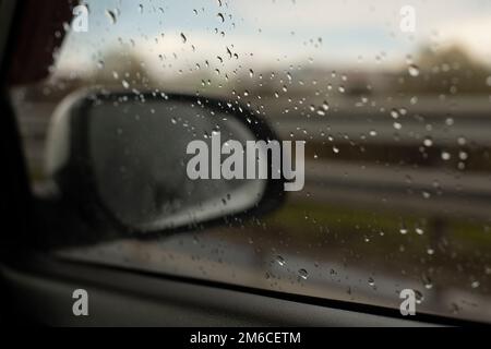 Rear-view mirror of car behind wet glass. Stock Photo