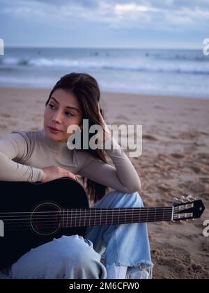 Young Woman with guitar sitting Close Ocean Stock Photo
