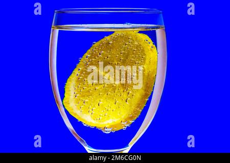 On a blue background, a glass with a lemon covered with gas bubbles Stock Photo