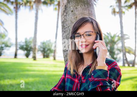 Attractive girl in eyeglasses talking on the phone while standing in a public park Stock Photo