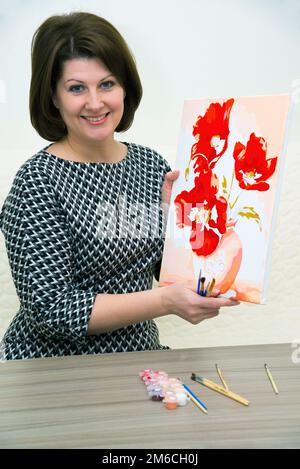 Woman is holding a painted picture with red poppies in her hands Stock Photo