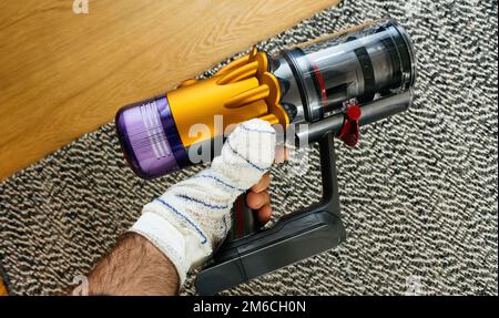 Personal perspective holding new cordless vacuum cleaner with empty bin ready to vacuum multiple dust particle, hair and other debris found on the parquet wood flooring Stock Photo