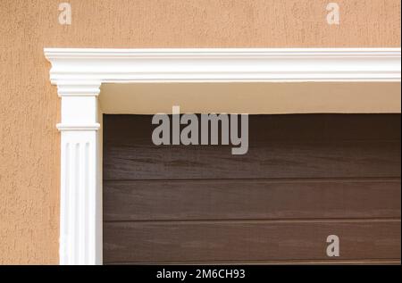 The brown metal garage door is decorated with a white arch of stucco for the background. Stock Photo