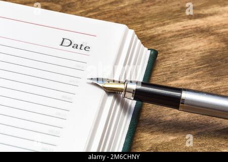 The word date on the page of the open diary and a fountain pen, close-up Stock Photo