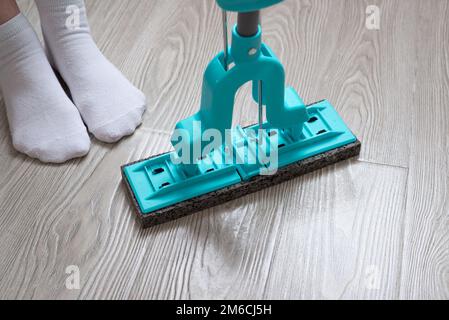 Female feet and blue mop on laminate background Stock Photo