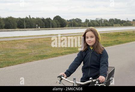 Cycling in the fall. A teenage girl on a bicycle rides along a water channel. Autumn motive. Stock Photo