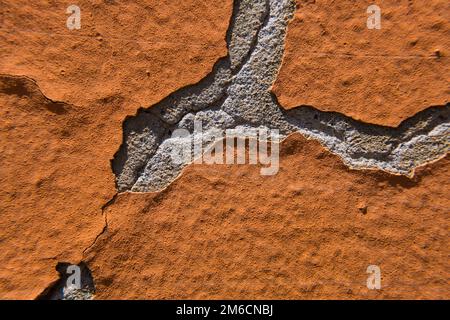 Orange peeling paint on a grey cracked concrete wall. Stock Photo