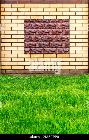 A rich wall of light brick decorated with a decorative brown stone and green lawn. Stock Photo