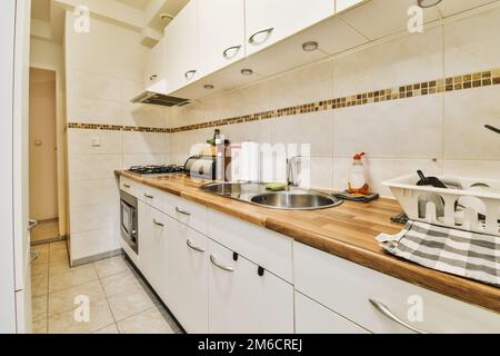 a kitchen with white cabinets and wood counter tops in the center of the image is an open door leading to another room Stock Photo