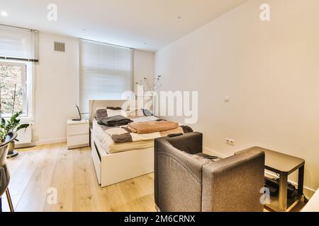 a living room with white walls and hardwood flooring, including a small bed in the corner of the room Stock Photo