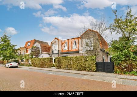 some houses on the side of a street with cars parked in front of them and green bushes growing along the road Stock Photo