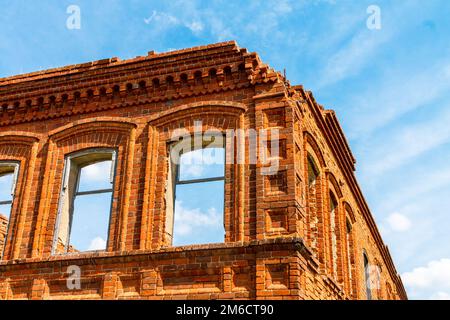 A large ruined ancient house of red brick against a blue sky with white clouds. Stock Photo
