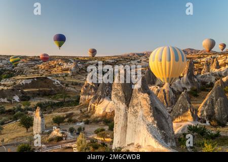 Hot air balloons flying at sunrise over rock formations in Cappadocia, Turkey Stock Photo