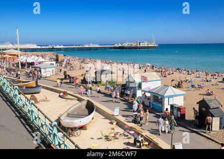 View of people enjoying the sunny summer weather on Brighton seafront promenade and beach with Palace Pier in the background, East Sussex, England, UK Stock Photo