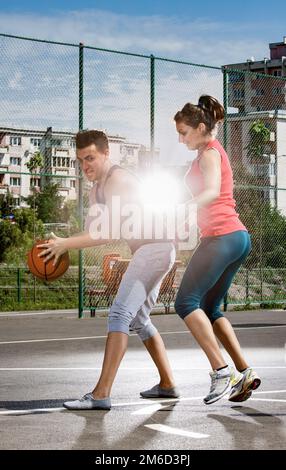 Young man and woman playing basketball on the playground Stock Photo