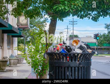 NEW ORLEANS, LA, USA - AUGUST 11, 2022: Full trash can on Oak Street in Uptown neighborhood Stock Photo