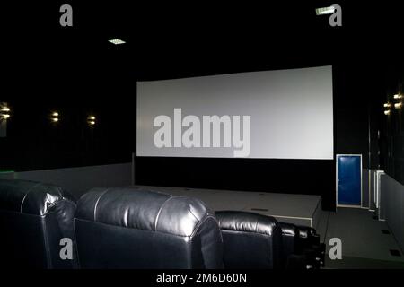The interior of a cinema hall with black leather seats and a white screen. The film does not show and no people. Stock Photo