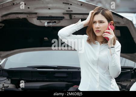 Young woman calling emergency help near broken car on road. Stock Photo