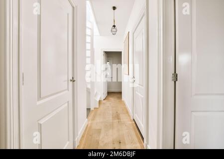 a long hallway with white walls and wood flooring the room is well lit by the light coming through the windows Stock Photo