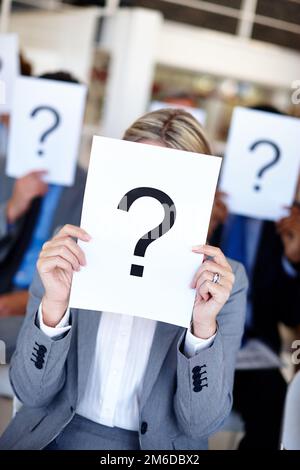 Can you answer our questions. a group of businesspeople holding up signs with question marks on them during a work presentation. Stock Photo