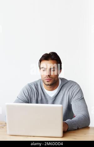 Seriously surfing the web. A handsome man sitting at a table and working on a laptop against a white background. Stock Photo