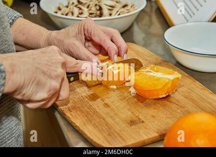 Chef cuts oranges to prepare salad with zucchini, oranges and salami. French gourmet cuisine, on a wooden background. Stock Photo