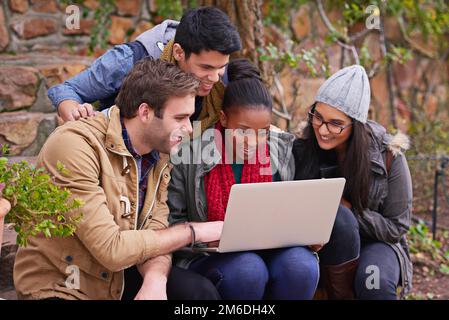Using technology to their advantage in their studies. a group of university students using a laptop while sitting on campus. Stock Photo