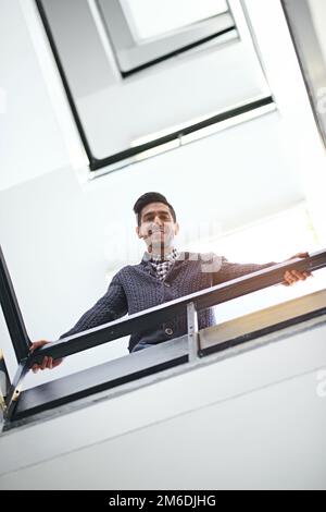 Hows it going down there. Low angle portrait of a young businessman leaning on a stairwell bannister. Stock Photo