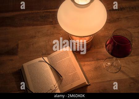 Open book old oil lamp and glass of red wine on wooden table Stock Photo