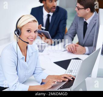 Nothing replaces hard work and diligence. Portrait of a positive businesswoman wearing a headset with staff members behind her. Stock Photo