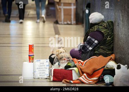 Homeless sits on the sidewalk with a blanket and two dogs, asks for charity. Milan, Italy - December 2022 Stock Photo