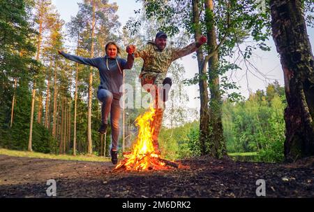 Young man and woman in a jump over a burning fire on the lake shore. Stock Photo