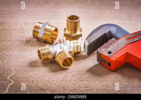 Brass Pipe Connectors And Monkey Wrench On Wooden Board Stock Photo