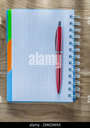 Checked spiral notebook pen on wood board. Stock Photo