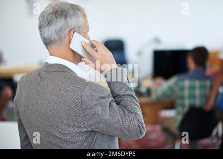 Ive just stepped into the office. a mature businessman talking on a cellphone while standing in an office. Stock Photo