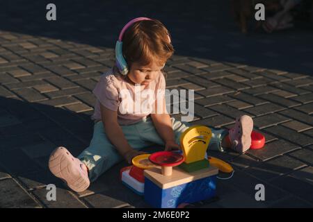 Little baby girl sitting on floor in the backyard playing with educational toy at sunny day in summer weekends. Having fun with colorful blocks Stock Photo