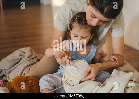 Mother with baby girl working with punch needles and embroidery hoop for needlework. Special tool for the tapestry and wool ball punching technique on Stock Photo