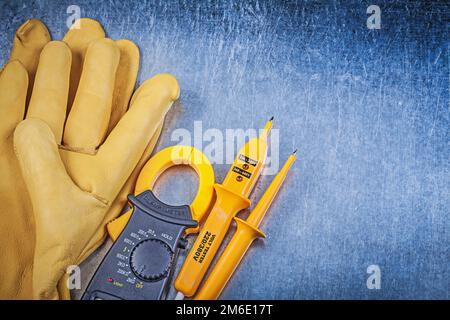 Composition of digital clamp meter electric tester protective gloves on metallic surface. Stock Photo