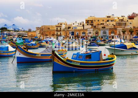 Traditional fishing boats luzzu in Marsaxlokk village in Malta, painted in bright colours – blue, red and yellow. Warm, afternoon sunlight Stock Photo
