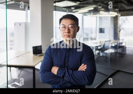 Portrait of asian businessman inside modern office, boss in glasses serious looking at camera, man with crossed arms thinking worker. Stock Photo