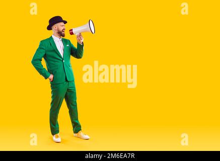 Man in green suit makes announcement through megaphone on yellow copy space background Stock Photo
