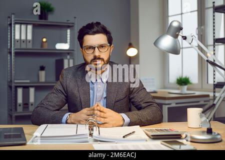 Serious confident businessman sitting at desk in modern office Stock Photo