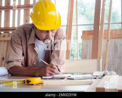 Happy senior carpenter using a tape measure for measuring woodwork in the carpentry workshop. Manufacture of wood products. Stock Photo