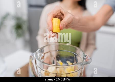 Cropped view of woman squeezing lemon above blender with fruits in kitchen,stock image Stock Photo