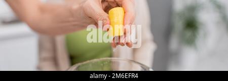 Cropped view of woman squeezing lemon above blender in kitchen, banner,stock image Stock Photo