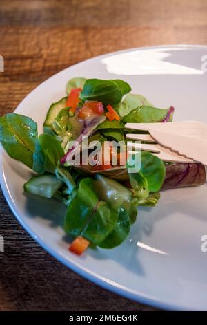 Environmentally friendly wooden cutlery on a plate with a side salad.  Alternative to less ecologically friendy single-use plastic in a cafe. Stock Photo