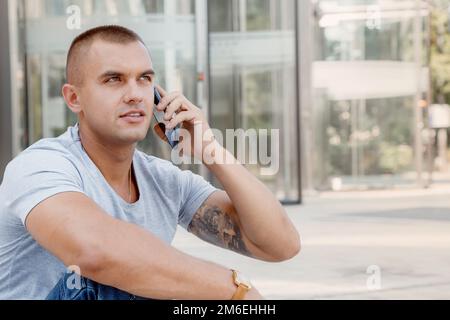 Young man talking on a cell phone. A guy with a tattoo on his arm. Handsome guy in the city. Stock Photo