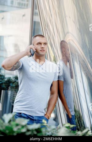 The man leans on a column. The guy is talking on the phone. Biceps tattoo. Man and cell phone. Stock Photo