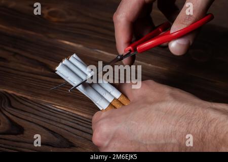 Quit smoking. Closeup of man hands holding bunch of cigarettes and cutting them in halves with scissors. Stop Smoking Cigarette Concept. Stock Photo
